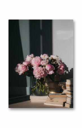 A glass vase of pink peonies on stacks of vintage books