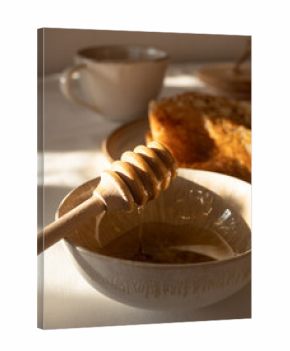 Composition of homemade thin pancakes on a beige ceramic plate with acacia honey in a jar and in a ceramic bowl with a wooden spoon and green tea in a beige ceramic cup on the table in the morning sun