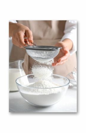 Fluffy white flour is being sifted through a metal sieve into a glass bowl, preparing for baking.