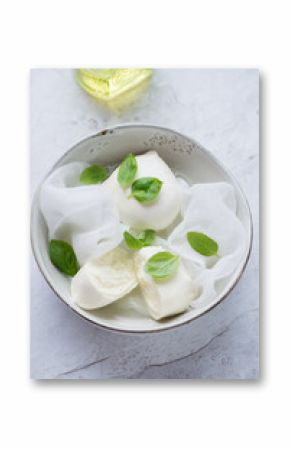 Bowl with freshly made buffalo mozzarella and green basil on a white stone background, elevated view, vertical shot