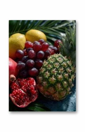 Fresh tropical fruits such as pineapple, pomegranate, grapes and lemons resting on wet palm leaf