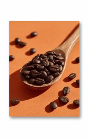 A wooden spoon filled with roasted coffee beans on orange background