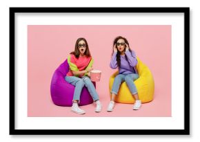 Full body young two friends shocked surprised amazed astonished women in 3d glasses watching movie film in cinema sit in bag chair isolated on pastel plain light pink color background studio portrait.