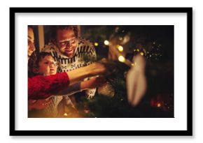 Happy family with mother, father, and child decorate Christmas tree in a cozy warm family home during winter holidays