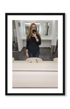 A woman is capturing a selfie while standing in front of a bathroom mirror
