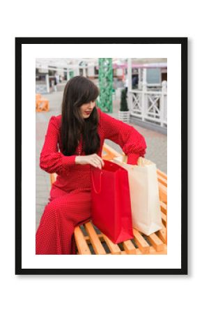 Woman smiles while reaching into shopping bag. Joy of shopping and discovering new purchases
