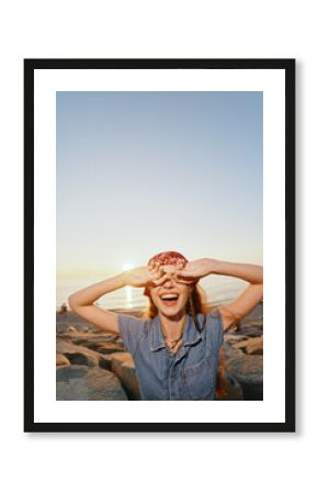 Lifestyle woman wearing modern boho-western denim street style laughing joyfully at sunset by the rocky shore with warm film color tones creating a relaxed vibe.