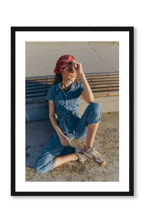 Lifestyle woman in modern boho-western denim street style wearing a red bandana, relaxed pose, natural sunlight, warm film color tone, casual outdoor setting.