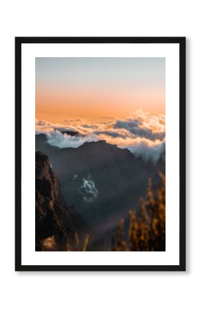 Sunset view of Pico do Arieiro mountain with vibrant orange sky and clouds behind the peak, dramatic mountain silhouette