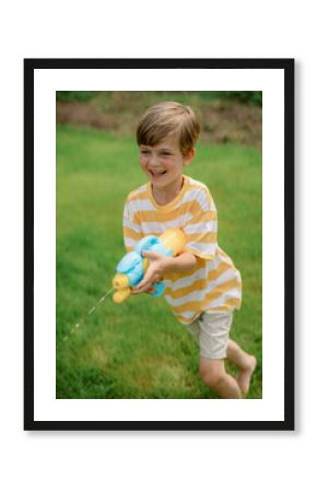 A young boy wearing a striped shirt and shorts joyfully runs across a green lawn while aiming a colorful water gun. The bright summer day enhances his playful spirit.