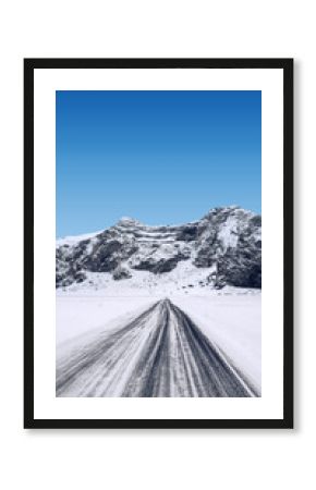 View of a long road stretches towards the snow-covered mountain under a bright blue sky on a winter day. Beautiful landscape for a natural or winter background or wallpaper