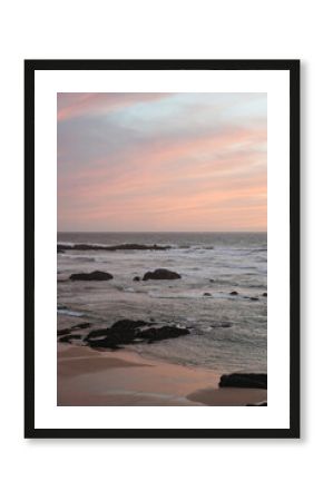 Rocky beach on the coast of Portugal. Waves, foam, pastel sky with pink and purple hues, peaceful scene, natural depth, sunset atmosphere.