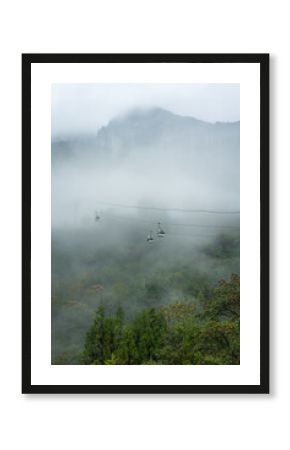 Cable cars travel through misty mountains in Yichang, China, above green forests reaching towards the sky.