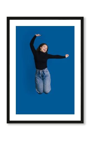 A Joyful Young Woman Jumping Against a Bright Blue Background, Exuding Energy and Happiness