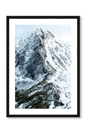Snow-covered mountain peak with rocky slopes and a cloudy sky. The landscape showcases winter scenery and natural beauty