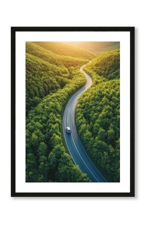 Aerial view of a car driving on a winding road through lush green forest at sunset in a scenic landscape