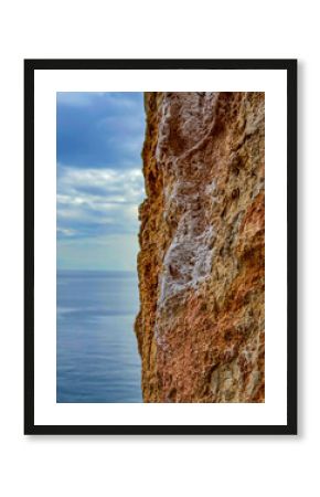 CLOSE UP, DOF: Detailed view of a textured limestone wall bearing white chalk marks left by climbers. Backdrop of sea and sky adds serenity and a nice color contrast to the rugged face of the rock.