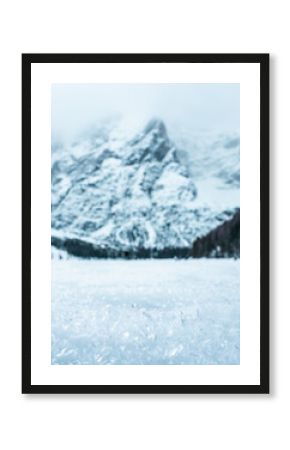 Close-up of ice crystals on frozen lake with snow-covered mountain and pine trees in background, cold winter scene 