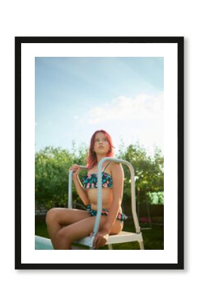 Teen girl relaxing at the edge of a pool in a colorful bikini while enjoying a sunny day outdoors