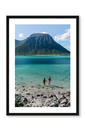 A couple stands hand-in-hand in the tranquil waters of a picturesque beach in Lofoten, Norway.