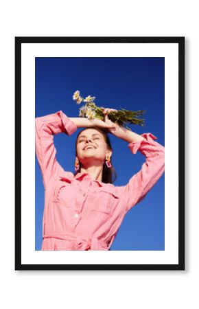 Joyful woman in a pink dress holding flowers, smiling against a clear blue sky, embodying themes of happiness and springtime freshness