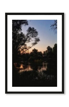 Peaceful sunset reflection on calm river surrounded by silhouette trees and natural landscape, warm evening light creating tranquil and serene atmosphere in nature, relaxing outdoor scenery.