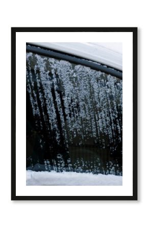 Frozen snow covers car window while streaks show where it has been scraped off on a cold winter morning