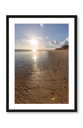 The golden sand beach of Praia da Falésia, crystal-clear sea water at low tide with the reflection of the sky, the setting sun, and the characteristic orange cliffs, Algarve, Portugal