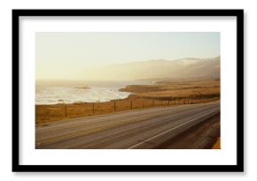 This is Route 1also known as the Pacific Coast Highway. The road is situated next to the ocean with the mountains in the distance. The road goes off into infinity into the sunset.