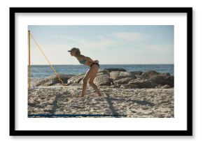 Volleyball player standing ready near yellow net post on sandy beach by rocky outcrop and ocean
