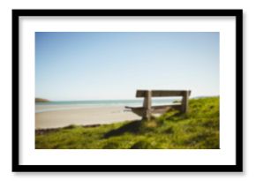 Empty bench by grass at beach