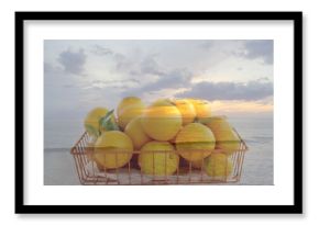 Sitting wire basket holding ripe oranges on sandy beach shoreline, with pastel sunset sky