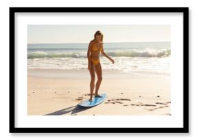 Blue surfboard is standing on damp sand at water's edge with surfing stance amid gentle waves