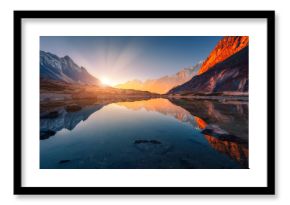 Beautiful landscape with high mountains with illuminated peaks, stones in mountain lake, reflection, blue sky and yellow sunlight in sunrise. Nepal. Amazing scene with Himalayan mountains. Himalayas