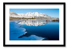 Maggies Peaks reflect in the calm water of Lake Tahoe and Taylor Creek in the winter near South Lake Tahoe, California.