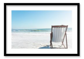 Person relaxing on wooden deck chair at beach shoreline, hand resting on striped seat, copy space
