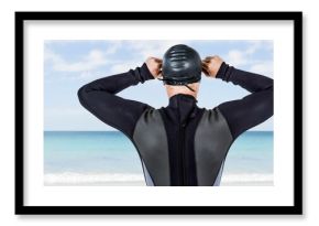 Male swimmer adjusting swimming cap while standing at beach