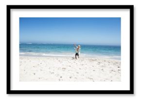 Boy kicking soccer ball at shoreline on white sand near turquoise ocean under clear sky