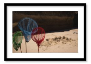 Three multicolored mesh nets are standing in sand on beach near dark rock and sand pile