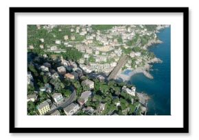Capturing pastel buildings clustering on steep terraced hillside by rocky shore with blue umbrellas