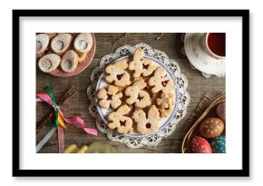 Homemade Linzer cookies in the shape of animals on a plate, with Easter eggs decorated with wax