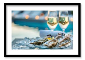 Romantic setting with plate of fresh oysters and two glasses of sparkling wine on terrace against sea