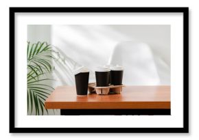 Takeout coffee cups placed on a wooden table next to a green indoor plant