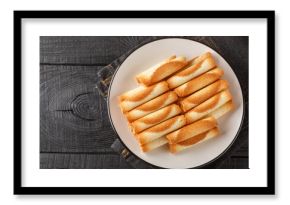 Cigarettes russes or russian cigarettes is a baked thin waffle rolls closeup on the plate on the table. Horizontal top view from above