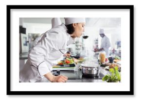 In a busy restaurant kitchen, chef tastes a steaming pan of soup, ensuring perfect seasoning of a great gourmet dish. Culinary workspace stocked with kitchen tools and fresh ingredients.