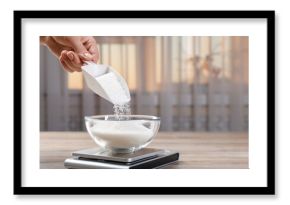 Woman adding sugar into bowl and digital kitchen scale at wooden table indoors, closeup. Space for text