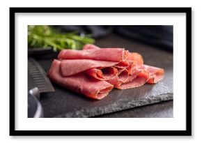 Sliced beef pastrami on cutting board on black table.