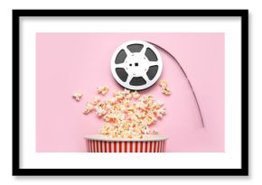 Bucket with tasty popcorn and film reel on pink background
