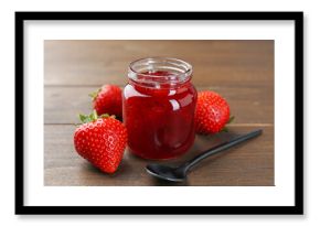Tasty homemade strawberry jam in glass jar and berries on wooden table, closeup