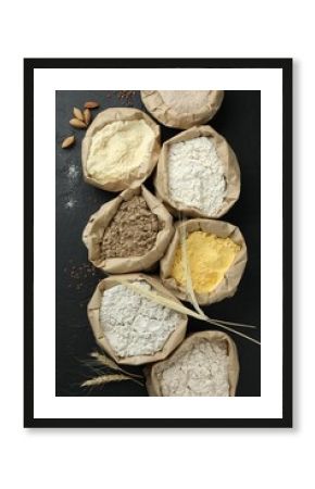 Different types of flour in paper bags on black table, flat lay